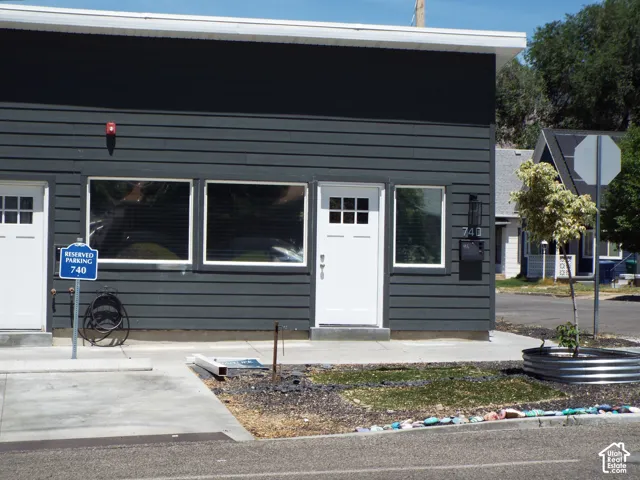 Modern exterior featuring dark horizontal siding, large rectangular picture windows, white-trimmed entry doors with multi-lite glass panels, and exterior wall-mounted lighting