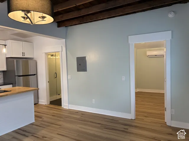 Interior space featuring exposed wooden ceiling beams, wood-finish flooring, a drum pendant light fixture, and a wall-mounted climate control unit