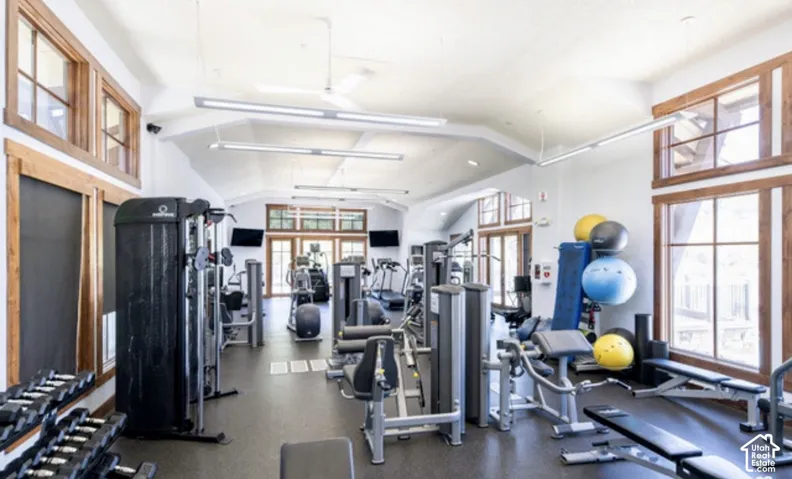 The work out room features vaulted ceilings, expansive windows overlooking the pool, wood trim, recessed lighting, and rubberized gym flooring
