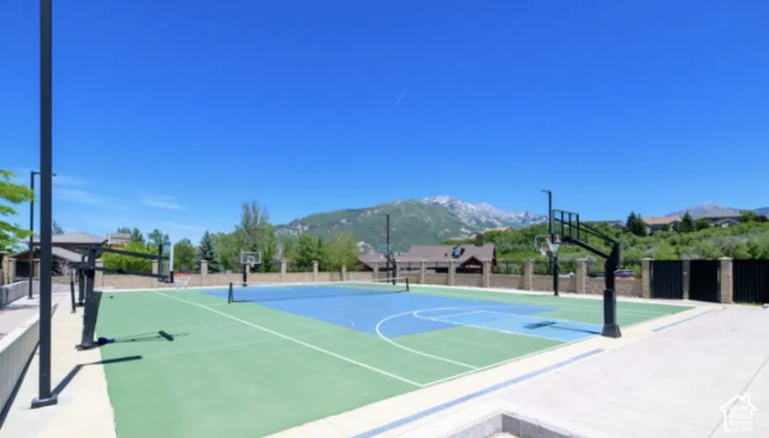 Multi-use sports court featuring a painted hard surface, integrated basketball hoops, tennis net system, perimeter masonry wall, and mountain backdrop