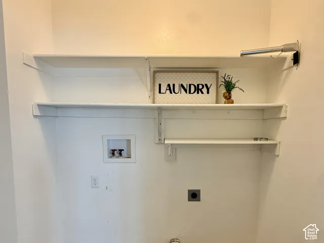 Dedicated laundry space featuring white built-in shelving, a mounted metal hanging rod, and recessed water hookups