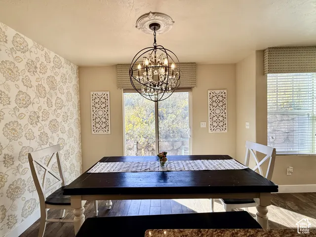 Dining space featuring a spherical crystal chandelier, ceiling medallion, wallpapered accent wall, wood-finish flooring, and a sliding glass door