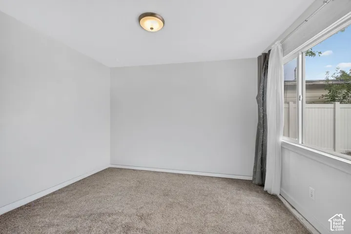 An empty bedroom off the back entry, with carpet and a large window onto the side yard.