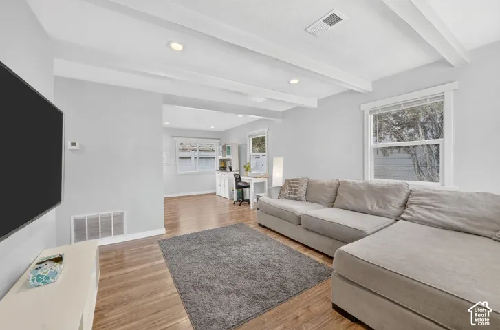 The living room has a painted beamed ceiling and laminate floors, with room for a large sectional and TV wall. It opens straight through to the dining area and a desk nook.