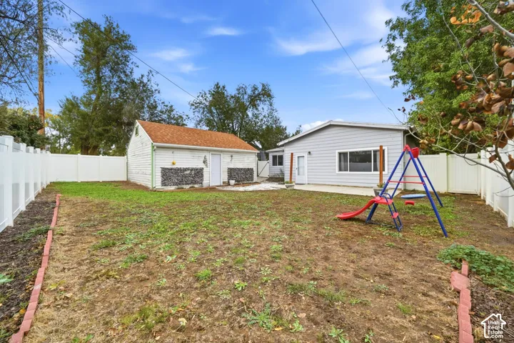 Another view of the fenced backyard, looking toward the garage and the back of the house. The lawn is flat, with a concrete patio by the house.