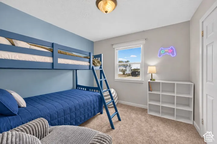 A bedroom with a blue accent wall and carpet, set up with bunk beds and a cube bookshelf. A window lets in daylight.v
