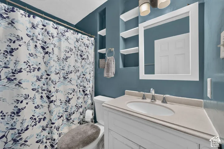 The bathroom sits off the hall beside the primary bedroom. It has built-in shelves next to the mirror and a vanity with an oval sink.