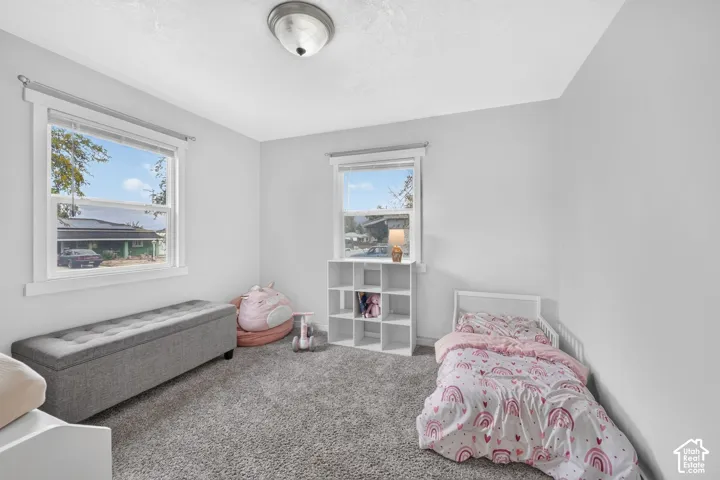A bedroom with carpet and two windows, with room for a twin bed, a cube bookshelf and a storage bench.