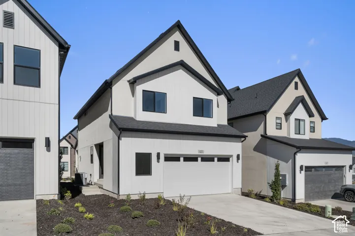 Modern architectural exterior featuring vertical and horizontal siding, a gabled roofline, multi-pane windows, and a concrete driveway