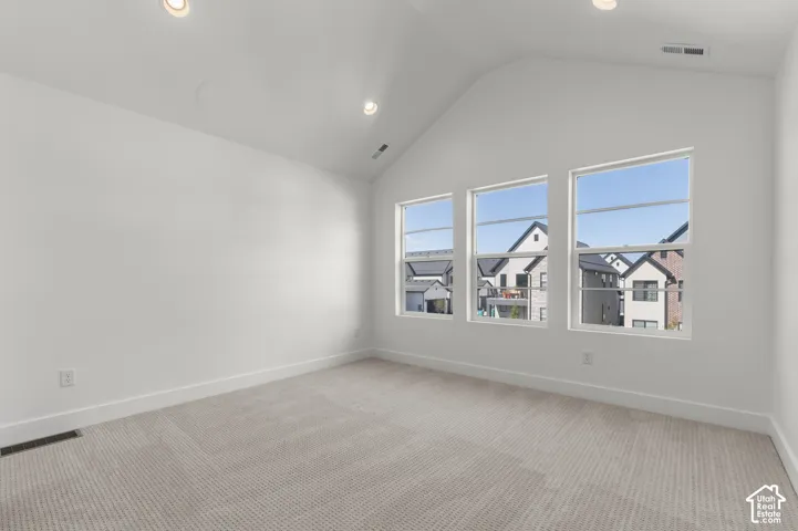Vaulted ceilings, neutral carpeting, and large windows providing natural light