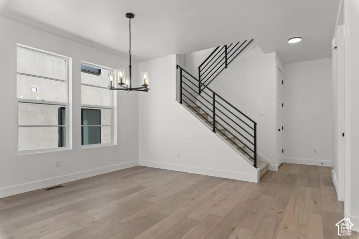 Open-concept interior featuring wood-finish flooring, a multi-light pendant fixture, and a staircase with a black metal horizontal railing