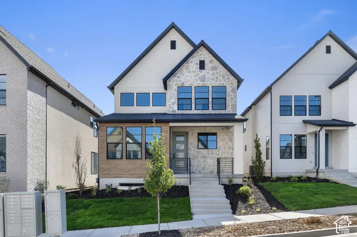 Two-story exterior featuring a mix of stucco and stone cladding, wood-finish paneling, multi-pane black-framed windows, and a concrete staircase with iron railings