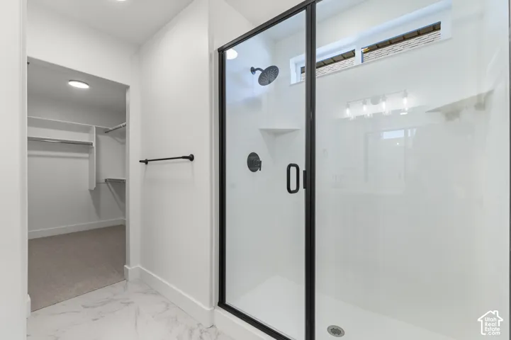 Walk-in shower with matte black fixtures, glass door enclosure, built-in shelving, and transom window, accompanied by a walk-in closet featuring white built-in storage and carpeting