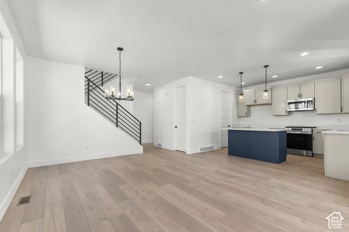 Open-concept area featuring wood-finish flooring, a kitchen island with a contrasting base, shaker-style cabinetry, recessed lighting, and a staircase with matte black horizontal railings
