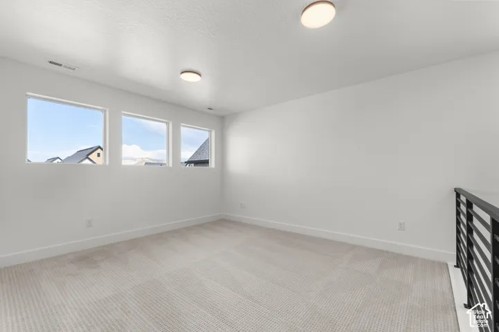 Neutral interior space featuring carpeted flooring, three expansive windows, flush-mount ceiling lighting, and a metal horizontal-bar railing