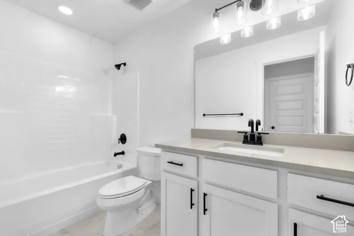 Bathroom featuring a quartz-topped vanity with matte black hardware, a shower-tub combination with white subway tile surround, and a large-format mirror with integrated lighting