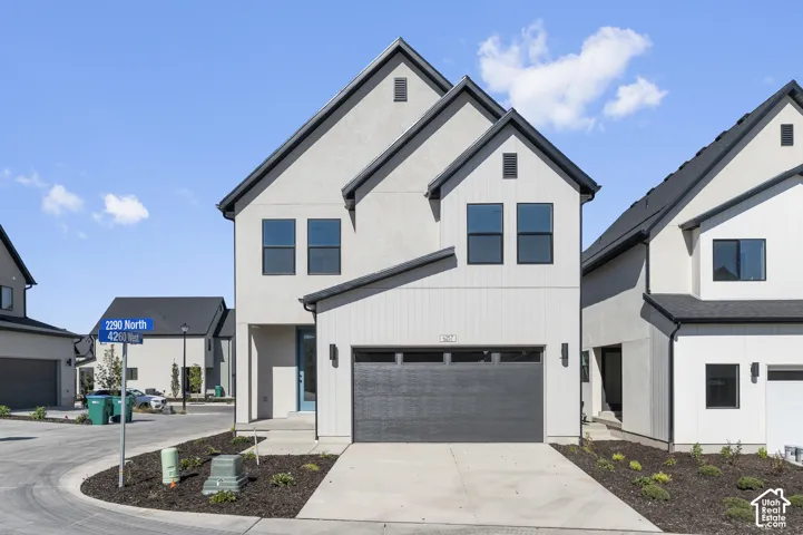 Two-story exterior featuring a neutral stucco and vertical panel siding facade, a dark asphalt shingle roof, integrated single-car garage, and concrete driveway