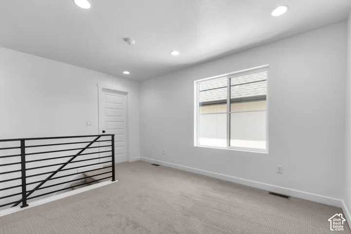 Neutral-toned carpeting, recessed LED lighting, a multi-panel interior door, and a metal horizontal-bar railing