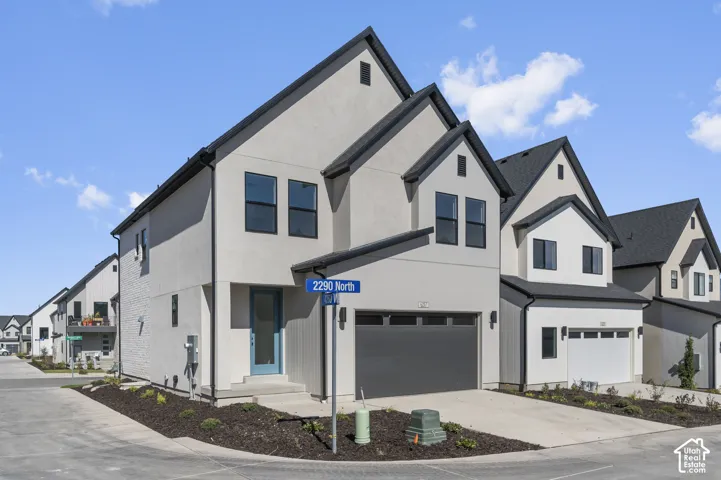 Two-story residence featuring a smooth stucco exterior, steeply pitched rooflines, black metal trim, and an attached two-car garage