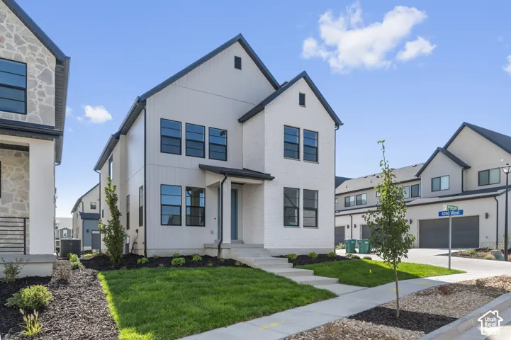 Modern multi-story exterior featuring white brick and vertical siding, dark window frames, gabled rooflines, and a concrete walkway
