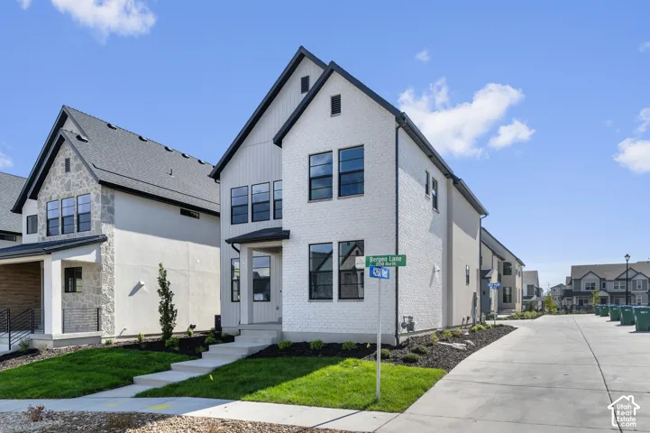 Two-story exterior featuring white brick and vertical siding, steep gabled rooflines, dark-framed windows, and concrete front steps