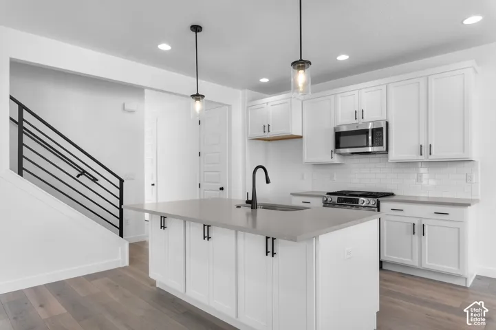Kitchen featuring white shaker-style cabinetry, quartz countertops, a subway tile backsplash, matte black hardware, and wood-finish flooring