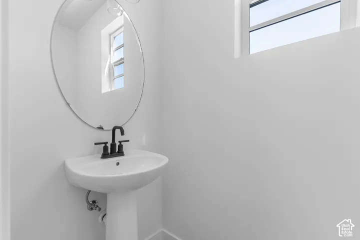 White pedestal sink with a matte black centerset faucet, oval frameless wall mirror, and dual horizontal windows