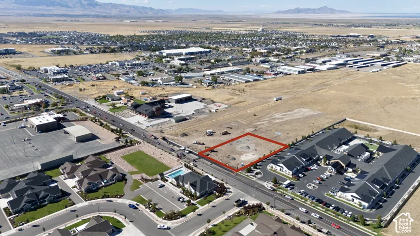 Expansive vacant land parcel featuring a level terrain, situated directly off a paved road, with commercial properties and residential buildings in the surrounding area