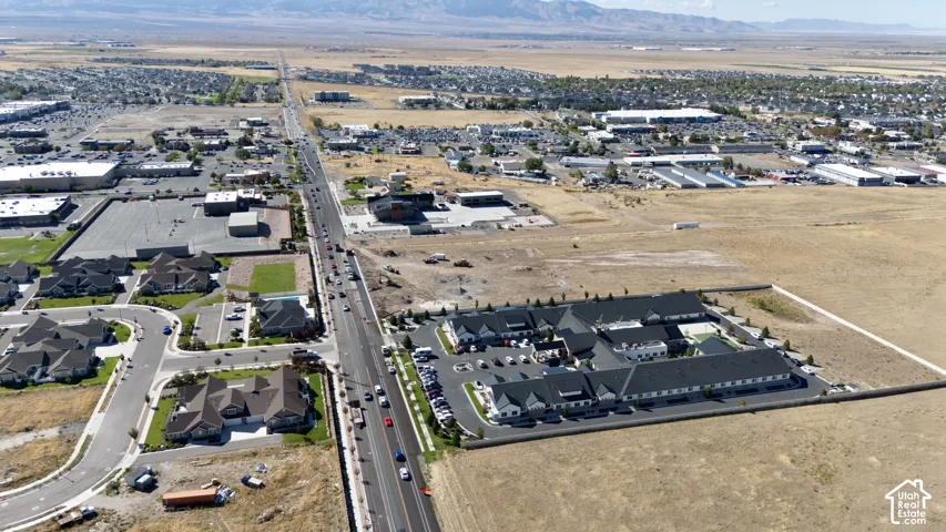 Expansive aerial perspective showcasing a developed commercial area, residential neighborhood, and extensive undeveloped land with mountain backdrop