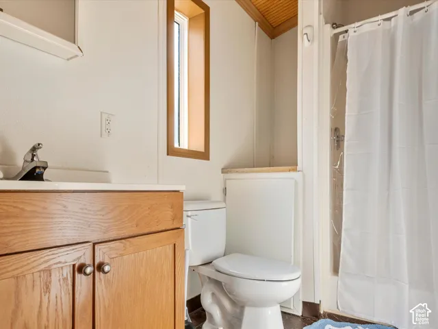 Bathroom featuring a wood-finish vanity with a single-handle faucet, vertical window with natural wood trim, beadboard ceiling accents, and a shower-tub combination