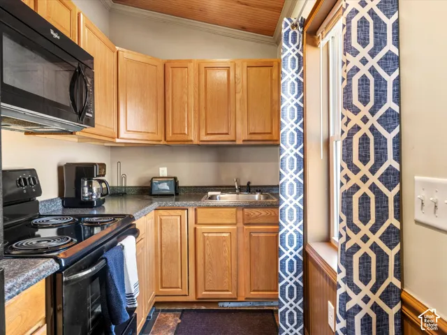 Kitchen featuring natural wood cabinetry, dark stone-finish countertops, stainless steel sink, black microwave, and a wood-plank ceiling