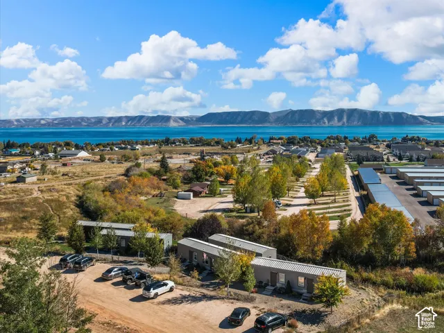 Aerial perspective of the property featuring linear residential structures, gravel parking areas, and a backdrop of expansive water and mountain terrain