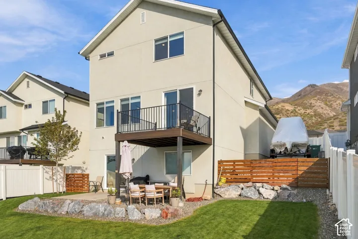 Stucco exterior with an elevated deck featuring black metal railing, concrete ground-level patio, wood-slat privacy fencing, and mountain backdrop
