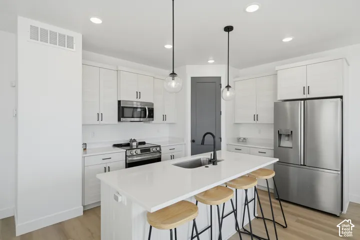 Kitchen featuring white shaker-style cabinetry, quartz countertops, stainless steel appliances, a center island with a matte black faucet, and pendant lighting