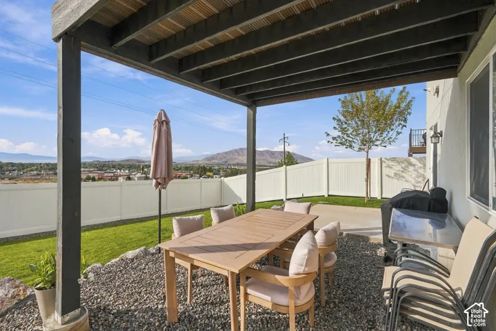 Covered patio featuring an exposed timber-beam ceiling, gravel ground cover, white vinyl fencing, and mountain backdrop
