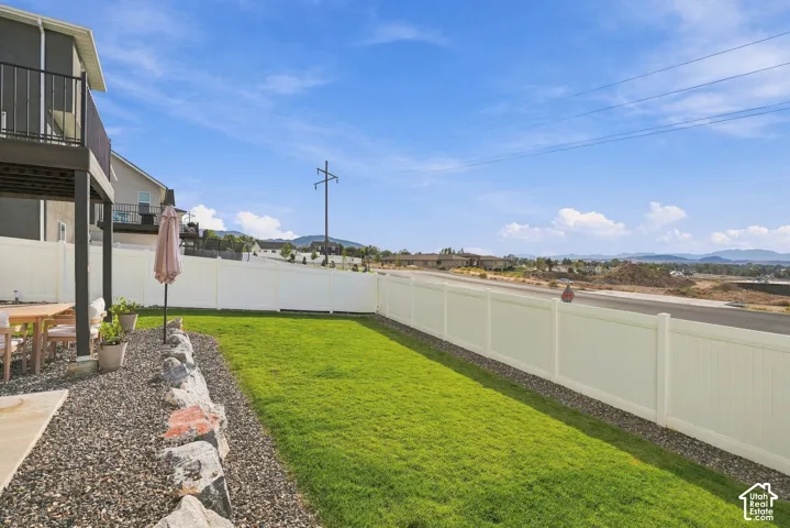 Backyard featuring a manicured lawn, white vinyl fencing, boulder hardscaping, and a covered concrete patio