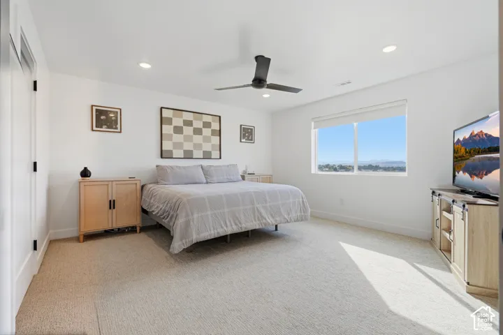 Neutral-toned carpeted flooring, recessed lighting, matte black ceiling fan, and large horizontal window with mountain backdrop