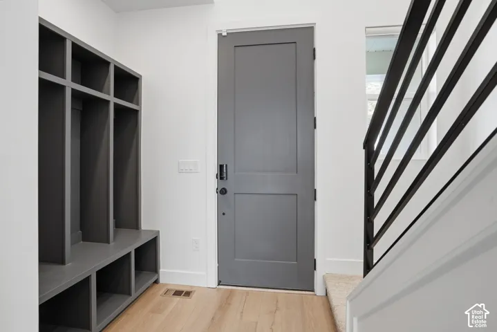 Entryway featuring a solid-core gray door, built-in mudroom cabinetry with integrated cubbies, and wood-finish flooring, complemented by a staircase with a horizontal matte black railing