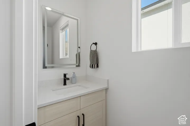 Vanity featuring light wood-finish cabinetry, quartz countertop, integrated rectangular sink, matte black faucet, and rectangular mirror with integrated lighting