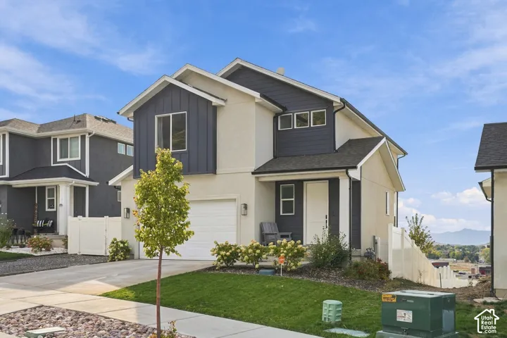 Two-story residence featuring a combination of light-toned stucco and dark vertical metal siding, an attached garage, asphalt shingle roofing, and a concrete driveway