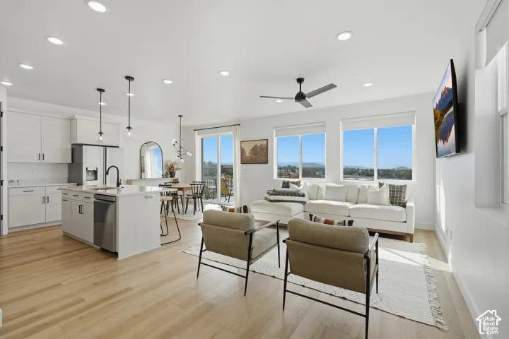 Open-concept kitchen and living area featuring wood-finish flooring, quartz-topped center island, matte black hardware, recessed lighting, and expansive windows