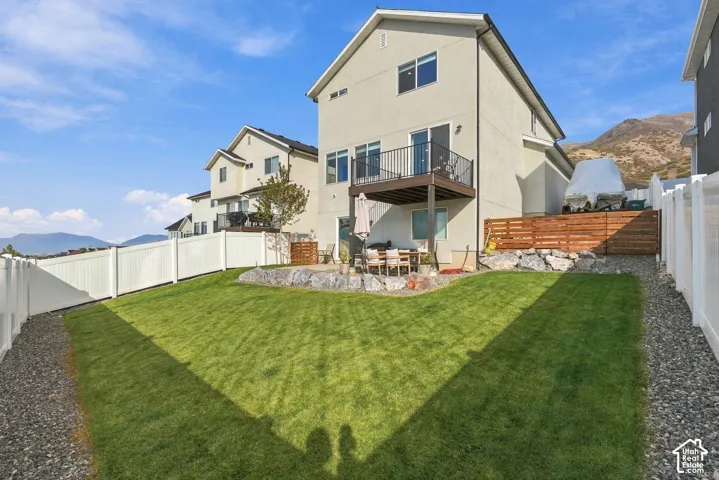 Rear exterior featuring an elevated deck with metal railing, stone-retaining wall, manicured lawn, horizontal wood privacy fencing, and mountain backdrop