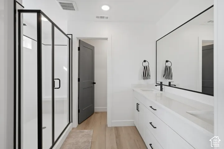 Dual-sink vanity with white cabinetry and quartz countertop, matte black fixtures, walk-in shower with glass enclosure and black framing, and wood-finish flooring