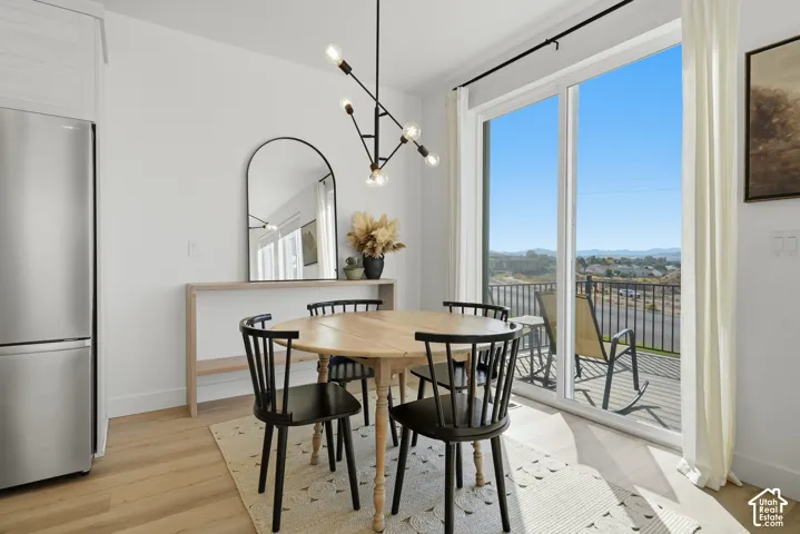 Modern dining area featuring wood-finish flooring, a stainless steel refrigerator, an industrial-style multi-arm chandelier, and sliding glass doors opening to a balcony with mountain scenery