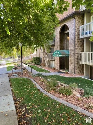 Brick exterior facade featuring arched entryway, decorative stone garden beds, manicured lawn, and multi-level balcony railings
