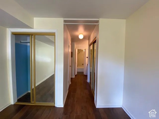 Hallway featuring wood-finish flooring, two closets with mirrored sliding doors, and a ceiling-mounted globe light fixture