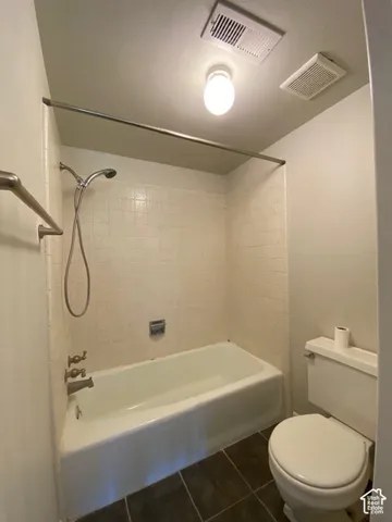 Full bathroom featuring a tub-shower combination with ceramic tile surround, handheld showerhead, wall-mounted metal towel bar, and dark-toned flooring