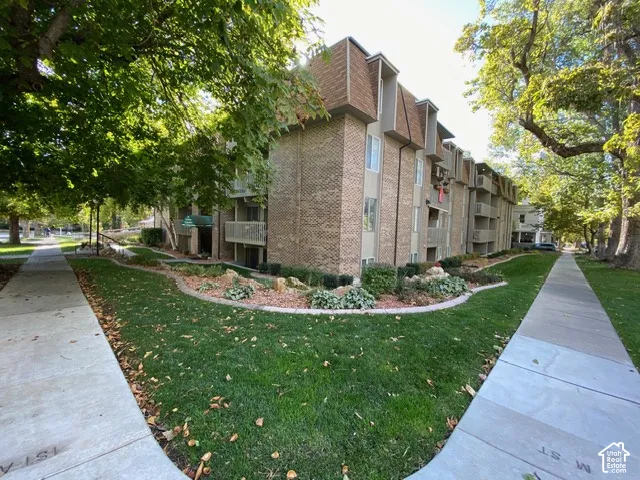 Multi-story brick exterior building featuring mansard roofing, integrated balconies, and landscaped grounds with mature trees