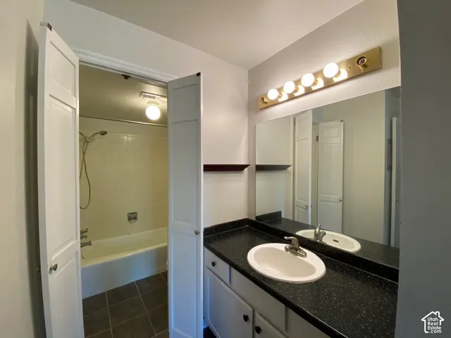 Bathroom featuring a dark solid-surface countertop with an integrated oval basin, white cabinetry, a large wall-mounted mirror, and multi-bulb vanity lighting