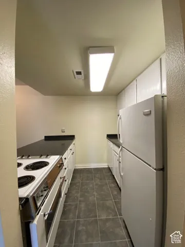 Kitchen featuring white cabinetry, dark solid-surface countertops, tile flooring, and integrated white appliances